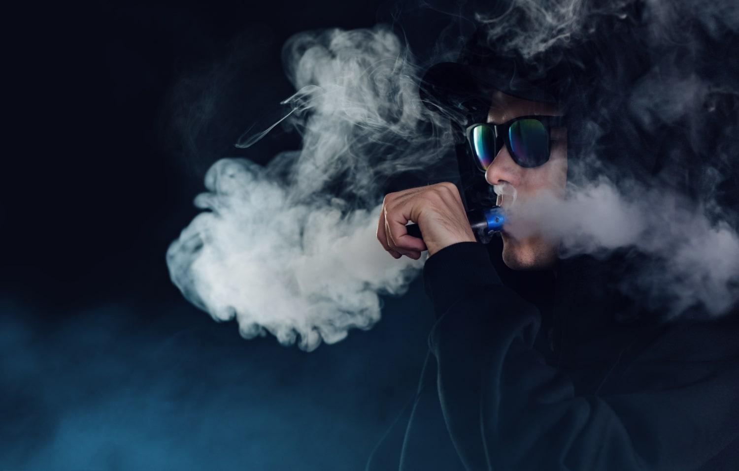 portrait handsome guy black hat sunglasses vaping exhaling cloud vapor from e cigarette min